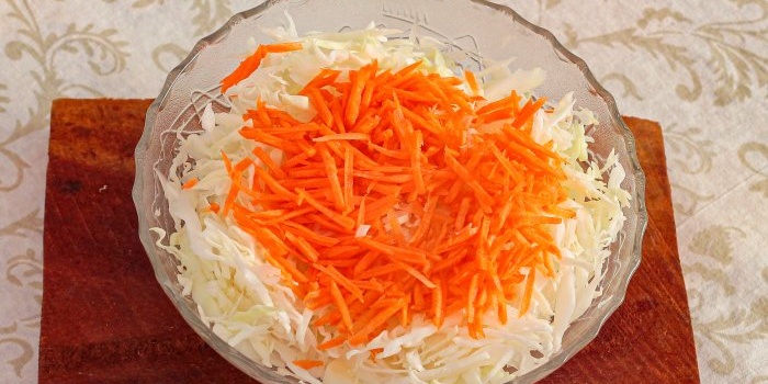 Geraspelte Karotten zum zerkleinerten Kohl geben