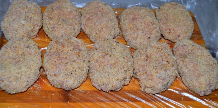 The cutlets are coated in breadcrumbs and placed on a cutting board in one row.